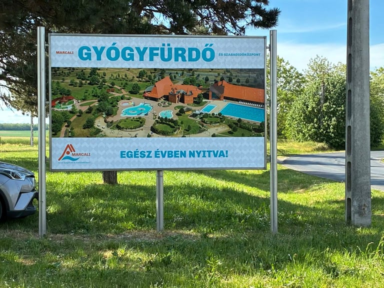 Roadside billboard advertising Gyogyfurdo resort in Hungary with image of swimming pools and buildings surrounded by trees