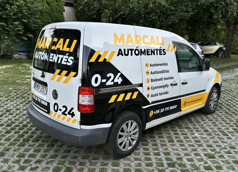 White and yellow Marcali Automentés service van parked on a brick driveway with green foliage background